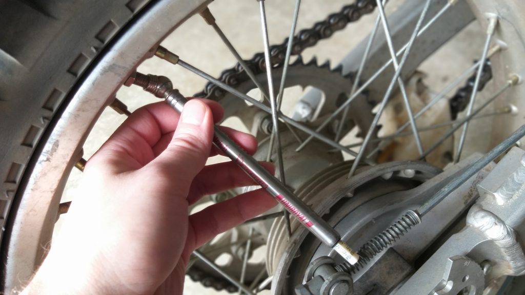 Checking dirt bike tire pressure with a pencil gauge. 