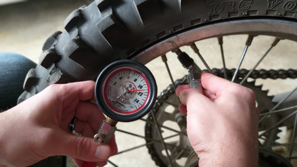 Checking dirt bike tire pressure with a quality pressure gauge.