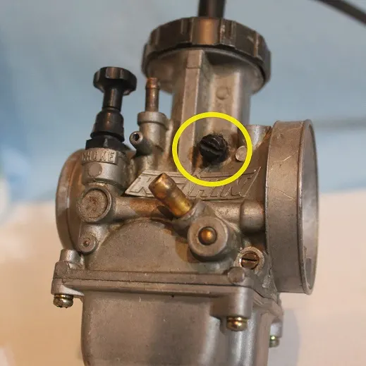 The idle speed screw on a dirt bike carburetor is usually on the left side near the middle