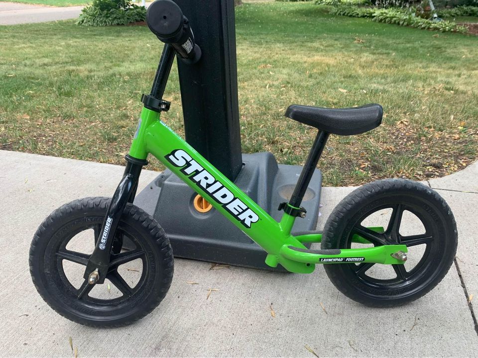 A green strider balance bike for toddlers and little kids